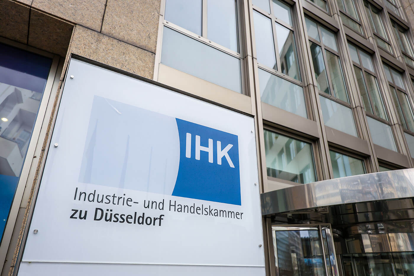 Vor  einem hohen Gebäude steht ein beleuchtbares Namenschild. Darauf steht "IHK Industrie- und Handelskammer zu Düsseldorf".
