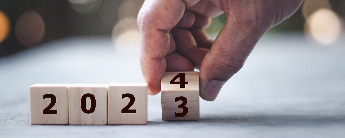 Das Foto zeigt vier Würfel, auf denen 2023 zu lesen ist. Der Würfel ganz rechts wird von einer Hand von 3 auf 4 gedreht.