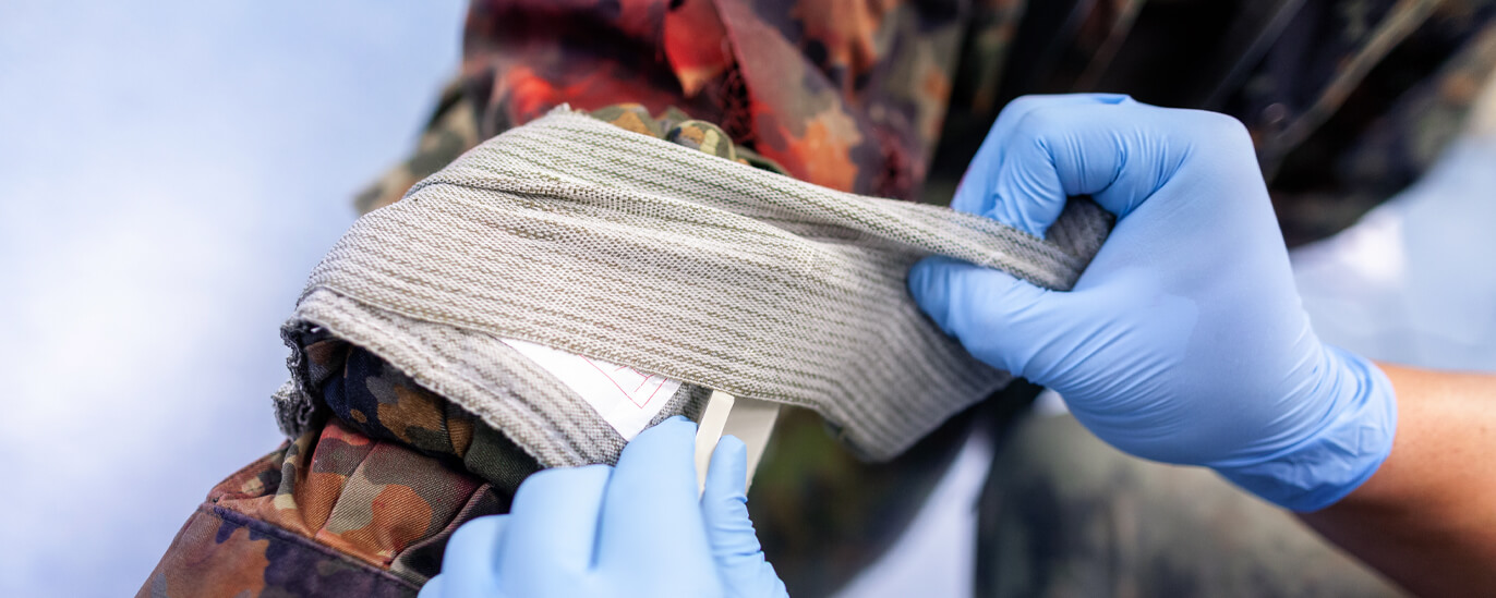 Person mit Handschuhen verarztet eine Verletzung eines Soldaten. 