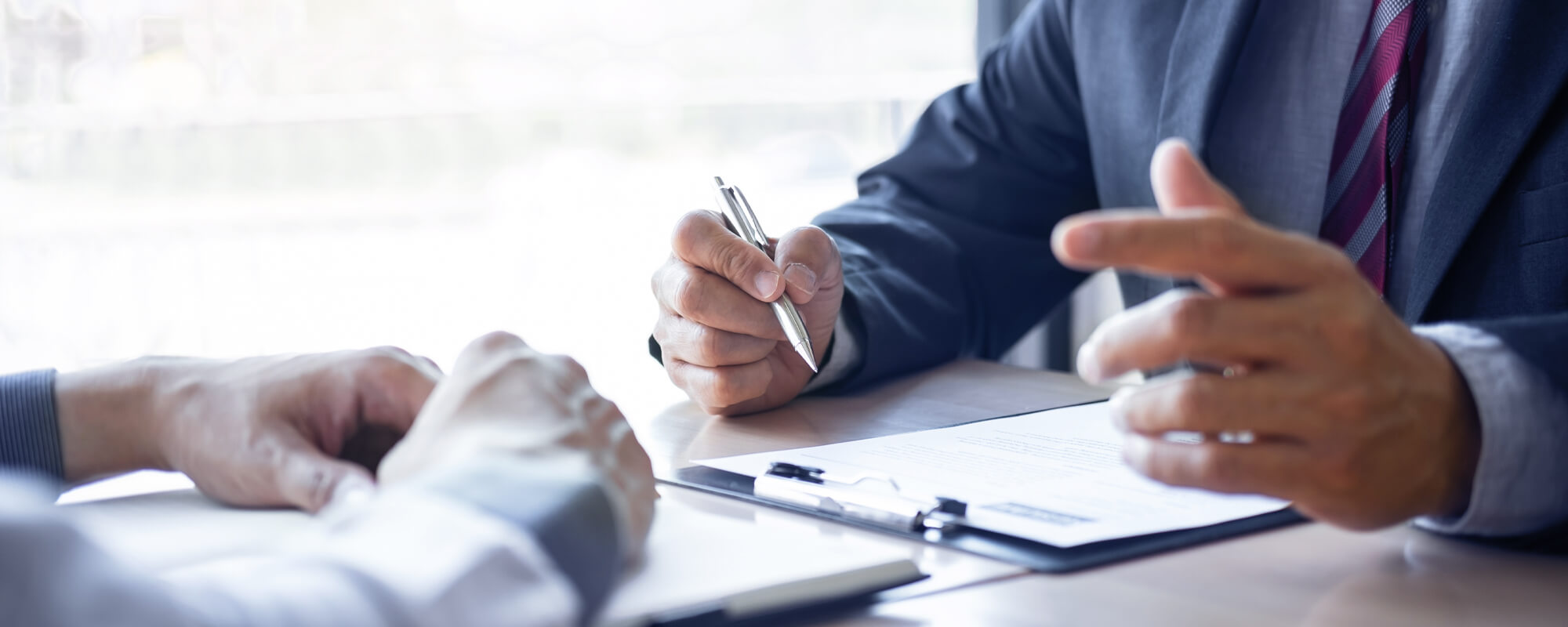 Beratungsgespräch zwischen zwei Personen am Tisch | © shutterstock / Elle Von Zwei angeschnittene Männer am Schreibtisch, die sich mit einander unterhalten und sich Notizen machen.