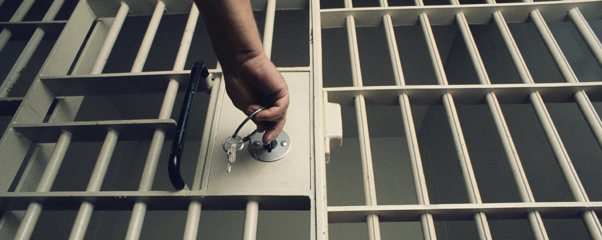 Person öffnet mit einem Schlüsselbund ein Gefängnisgitter. 