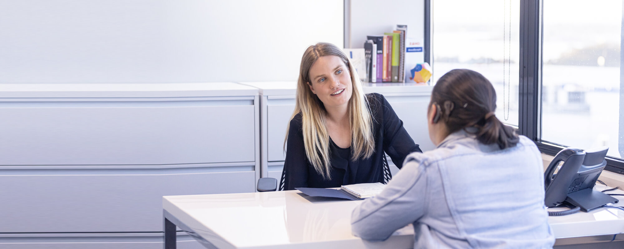 Frau spricht mit Gehörloser am Schreibtisch | © gettyimages / ImagePatch Eine blonde Frau spricht mit einer gehörlosen Frau am Schreibtisch und lächelt.