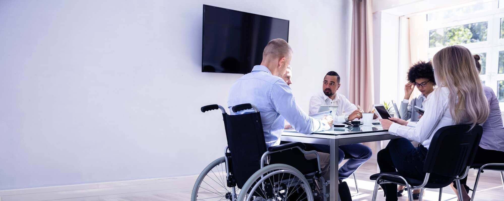 Rollstuhlfahrer sitzt mit Kollegen in einem Konferenzr