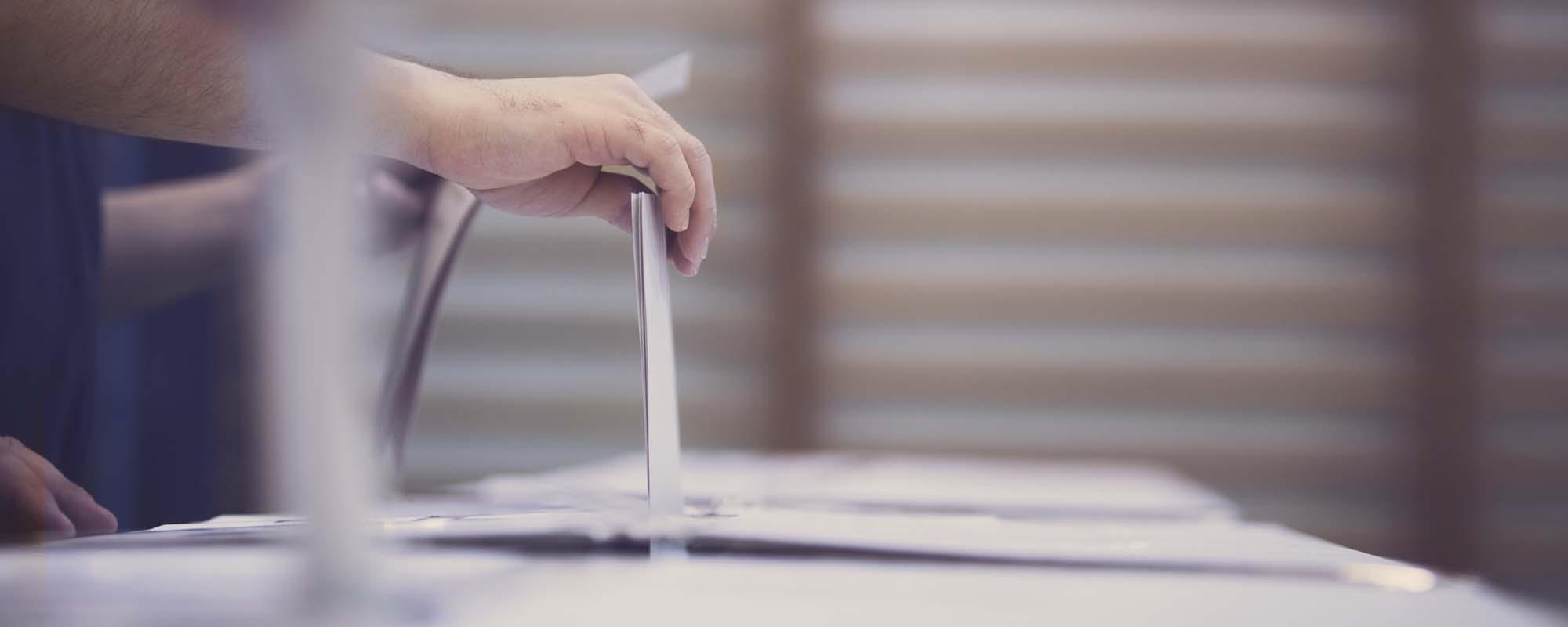 Person wirft Wahlzettel in Urne | © shutterstock / Alexandru Nika Person hält in der Hand einen Wahlzettel über dem Schlitz der Wahlurne.