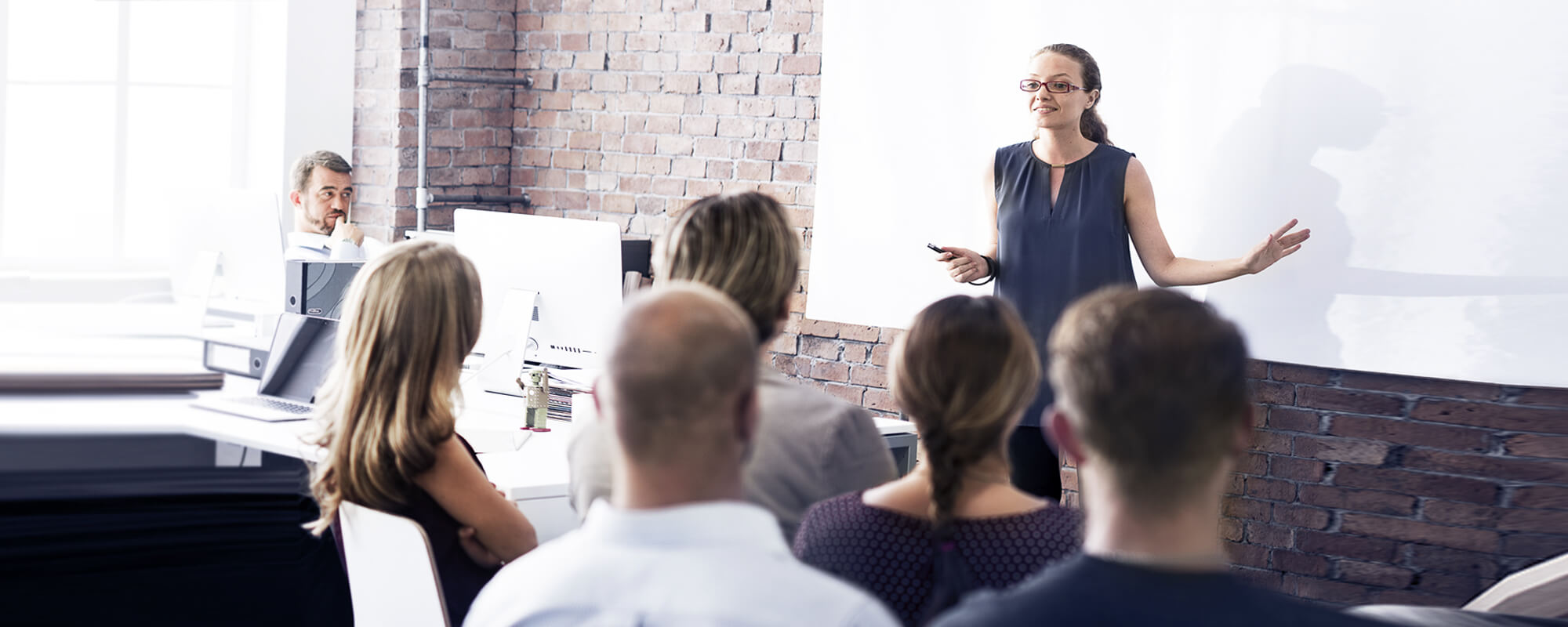 Eine Dozentin steht vor einer weißen Tafel und hält ein Seminar ab