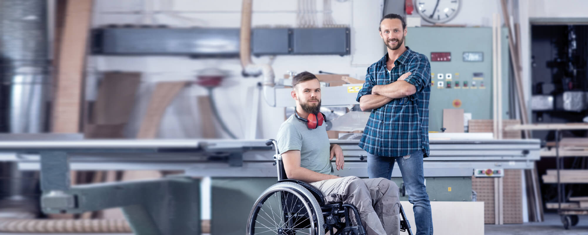 Behinderter Rollstuhlfahrer in einer Werkhalle mit seinem Kollegen.