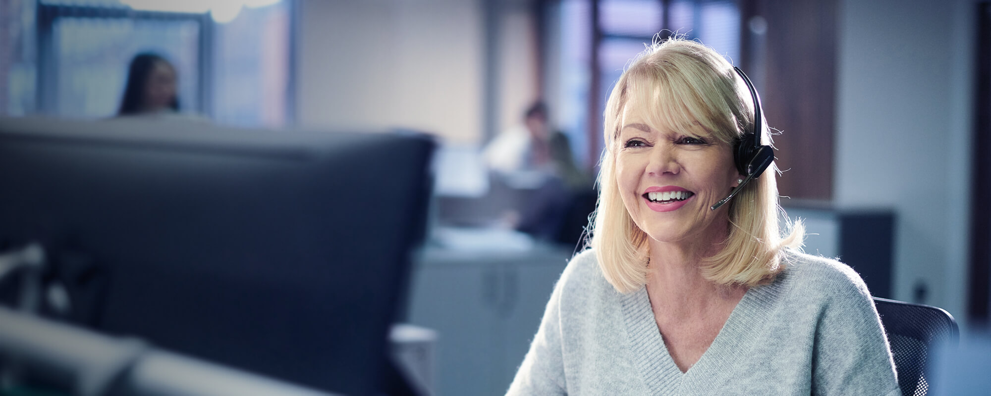 Blonde Frau telefoniert in einem Büro mit dem Headset. 