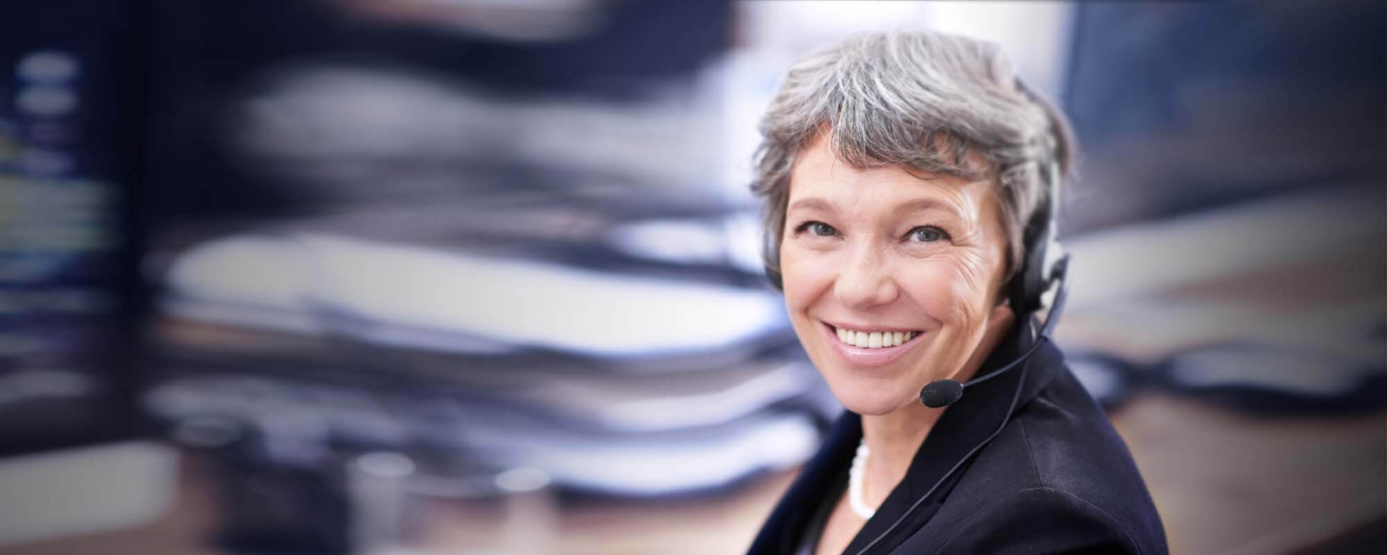 Lächelnde Frau mit Headset sitzt im Büro. 