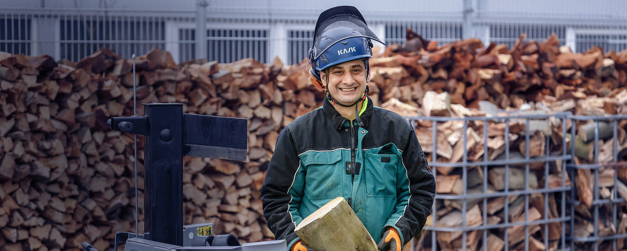 Ein Mann mit Helm und Arbeitskleidung spaltet Holz
