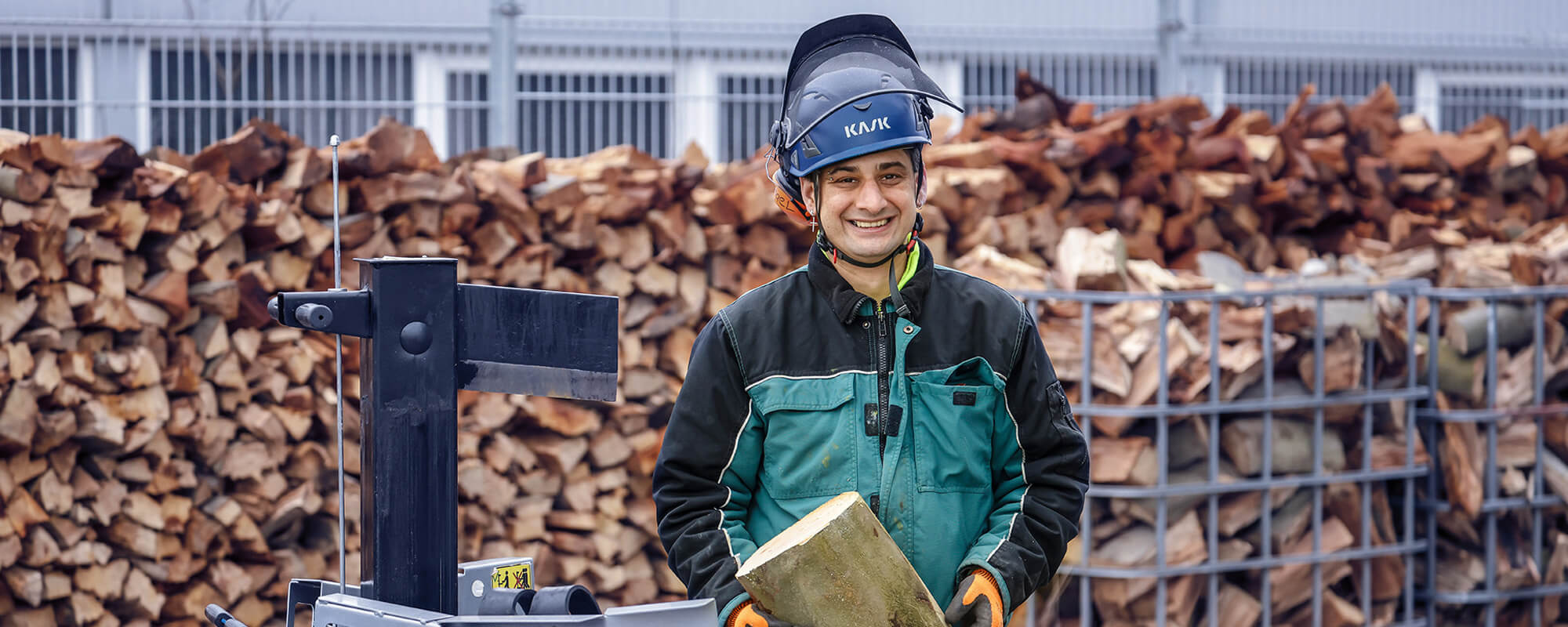 Ein Mann mit Helm und Arbeitskleidung spaltet Holz