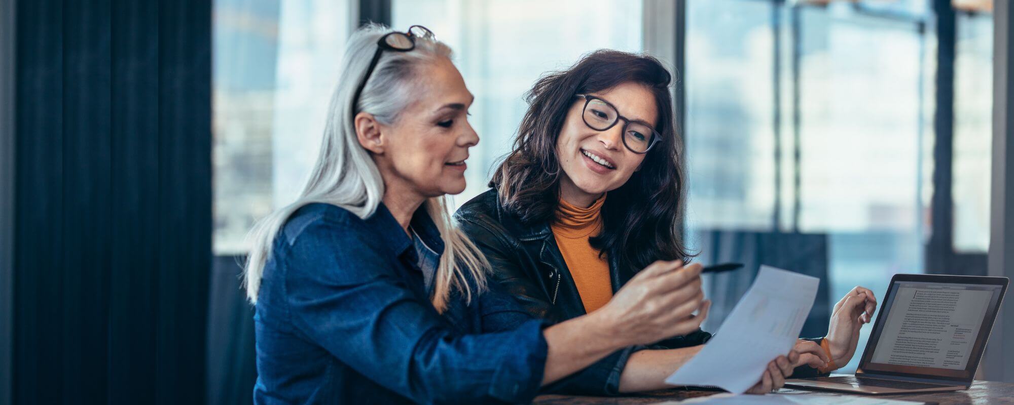 Betriebliches Eingliederungsmanagement | © Shutterstock Zwei lächelnde Frauen sitzen im Büro vor einem Notebook.