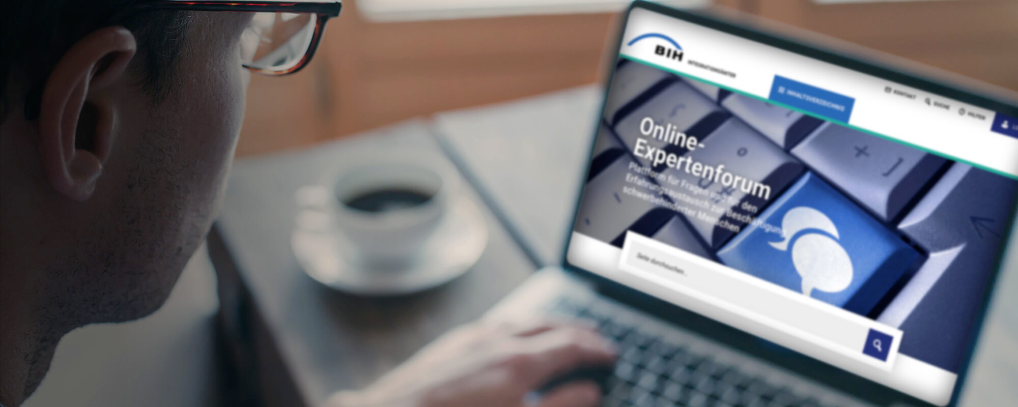 Das Foto zeigt einen Mann, der am Laptop arbeitet. Der Blick fällt von hinten über die Schulter auf den Monitor. Darauf ist eine große Tastatur mit zwei Sprechblasen auf einer der Tasten zu sehen.