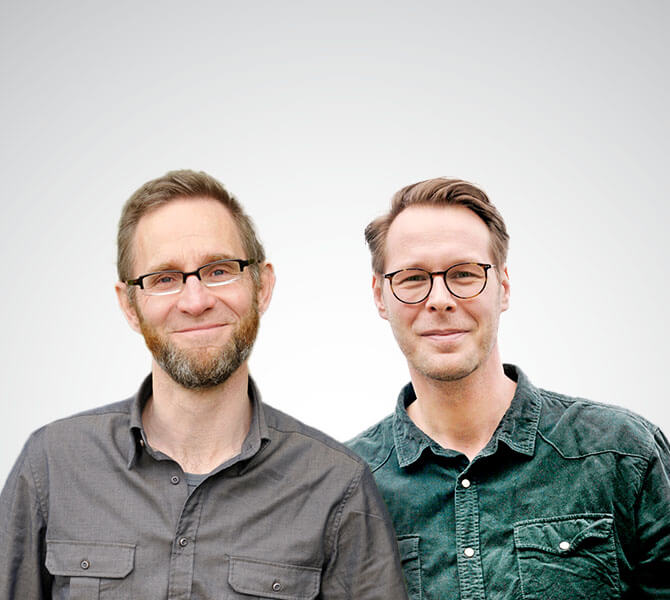 Das Foto zeigt die beiden Jobcoaches am Arbeitsplatz, Sven Kornwinkel (links) und Thomas Henke, vor einem neutralen grauen Hintergrund.