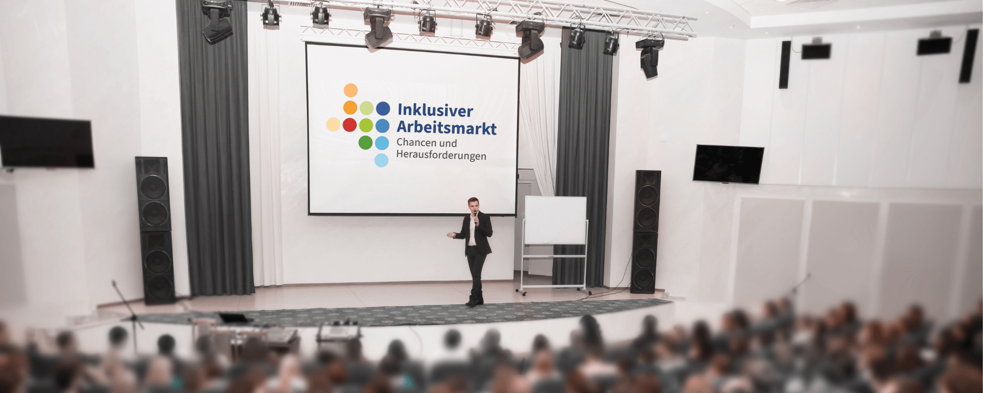 Das Foto zeigt einen großen, vollbesetzten Veranstaltungsraum. Auf der Leinwand im Bühnenbereich ist das Logo des Forums mit der Beschriftung eingeblendet: Inklusiver Arbeitsmarkt, Chancen und Herausforderungen