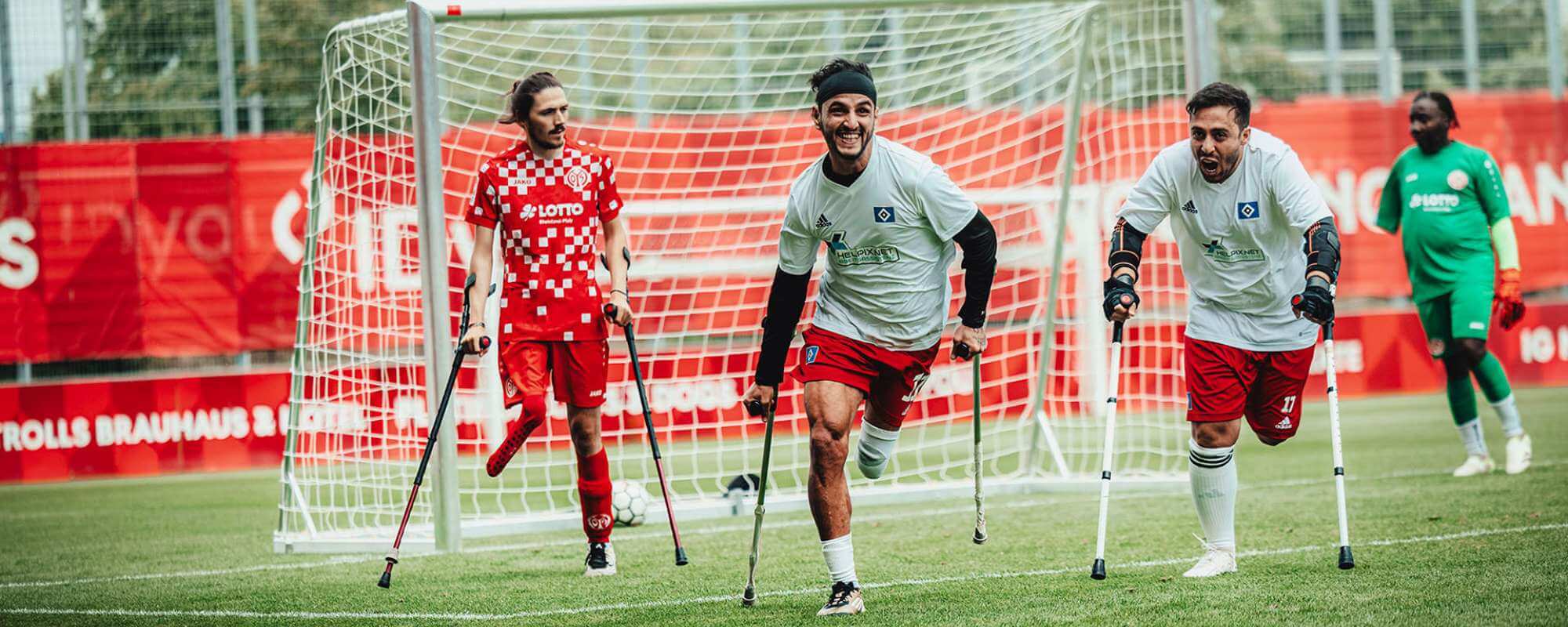 Das Foto zeigt drei beinamputierte DAFL-Fußballspieler vor dem Tor. Auf Unterarmstützen rennen sie aus voller Kraft dem Ball entgegen. Der Linienrichter ist armamputiert.
