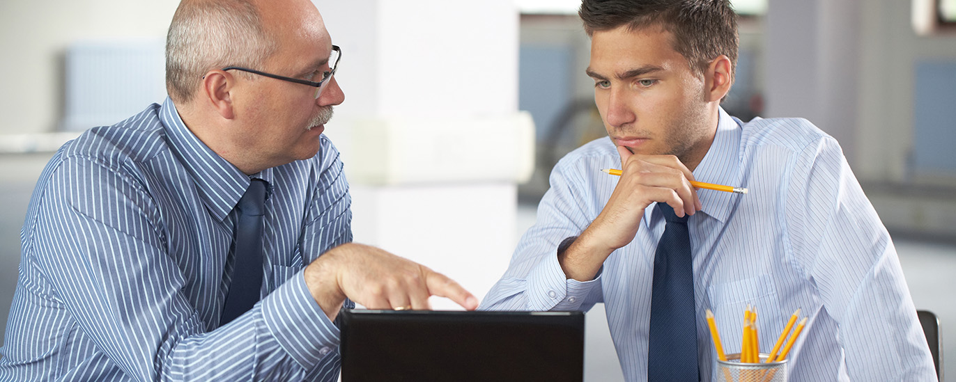 Datenschutzbeauftragte können nicht gleichzeitig Vertrauensperson sein. | © Michal Kowalski/Shutterstock Ein älterer Mann und ein jüngerer Mann befinden sich in einem Gespräch. Der ältere Mann zeigt auf einen Laptopbildschirm, der vor ihm steht.