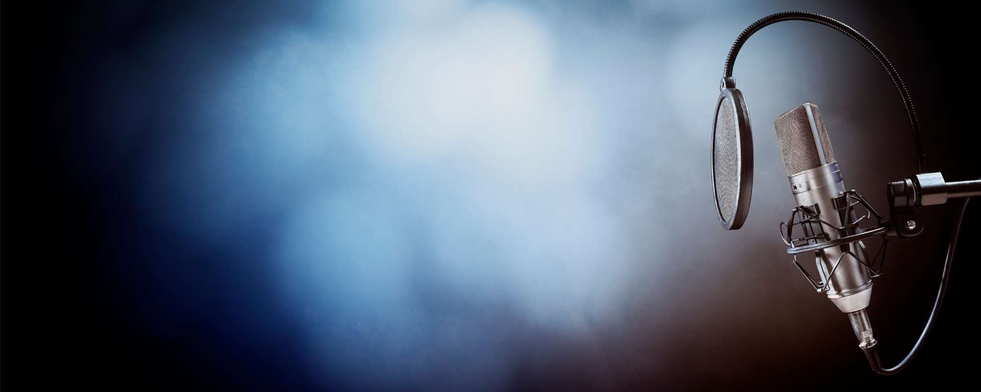 Das Foto zeigt ein Studiomikrofon vor blauem Hintergrund mit Scheinwerferlicht. Das Licht fällt auf das Mikrofon