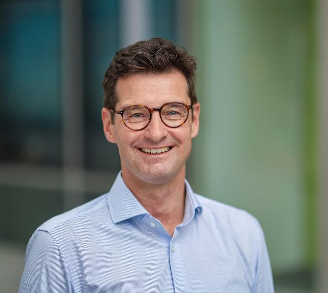 Porträtfoto von Christoph Beyer, ein Mann mittleren Alters mit Kurzhaarschnitt und Hornbrille. Er trägt ein hellblaues Hemd mit offenem Kragen und lächelt offen.