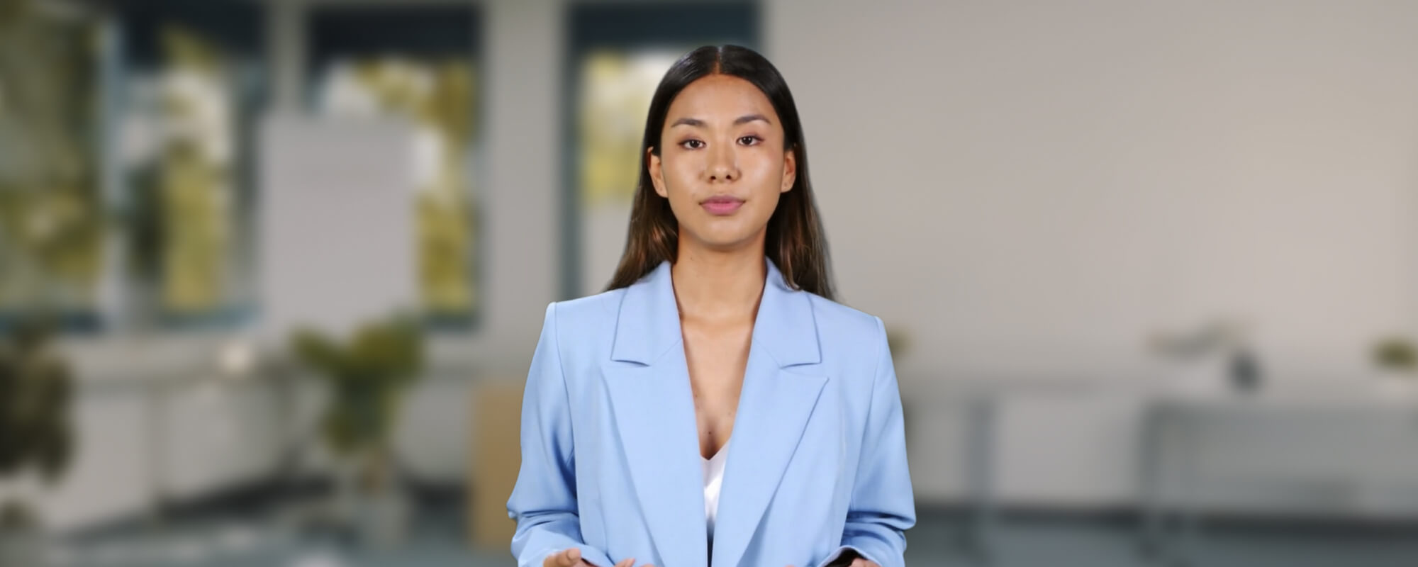 Ein Avatar, junge dunkelhaarige Frau in hellblauem Sakko, steht in einem moderne Büro mit Grünpflanzen.