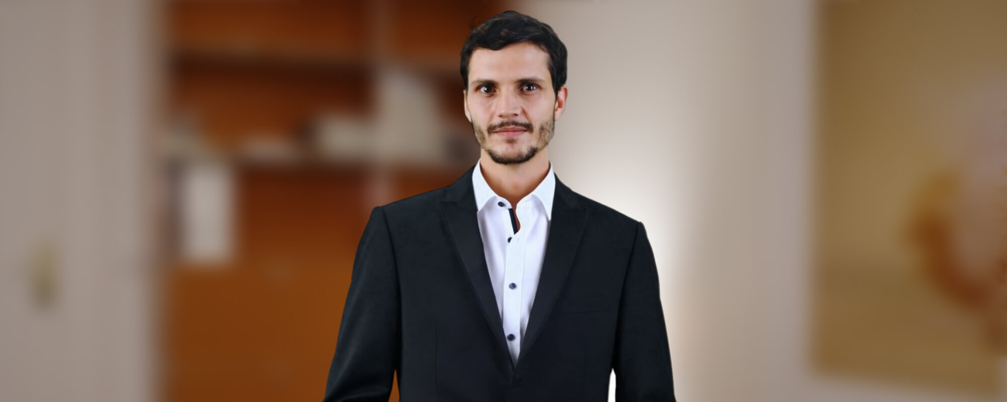 Ein Avatar, jüngerer Mann in dunkelblauem Anzug, steht in einem Büro vor einem hohen Bücherregal aus rotem Holz.