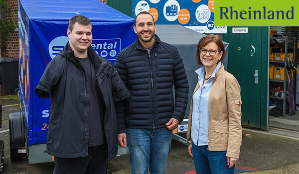 Das Foto zeigt drei Personen vor einem offenen Betriebsgebäude. Dem jungen Mann links im Bild fehlen die Arme. Sein Vorgesetzter und eine EAA-Beraterin stehen lächelnd neben ihm. 