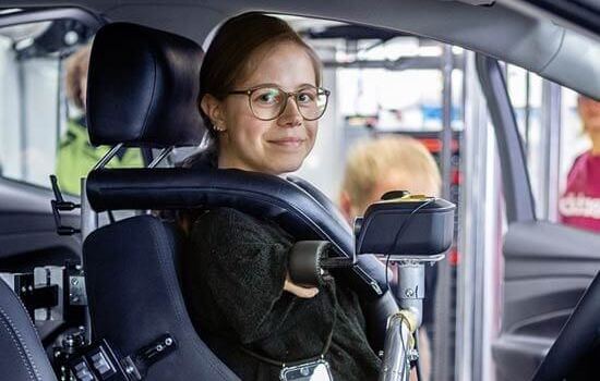 Eine junge Frau sitzt in einem behindertengerecht umgebauten Auto.