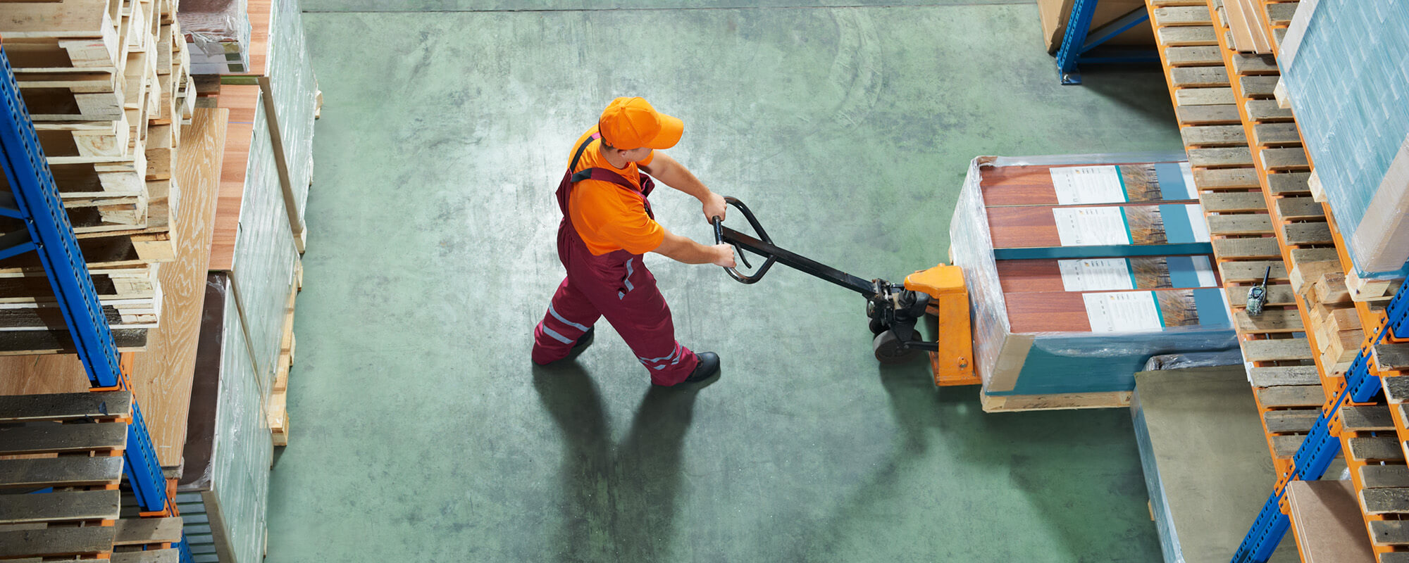 Ein Mann in oranger Arbeitskleidung bewegt mit einem Elektrohubwagen Kisten mit Laminat. 