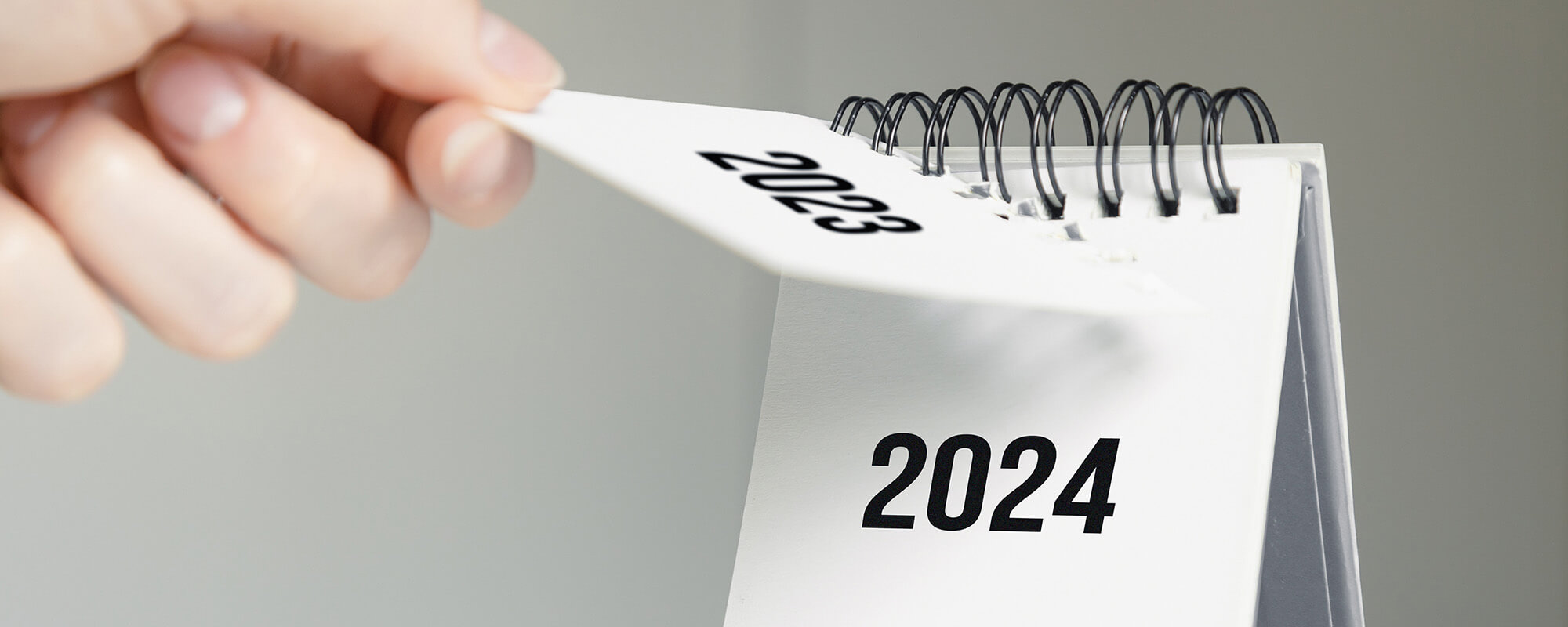 Auf einem weißen Tischkalender reißt eine Person das Blatt mit 2023 ab.