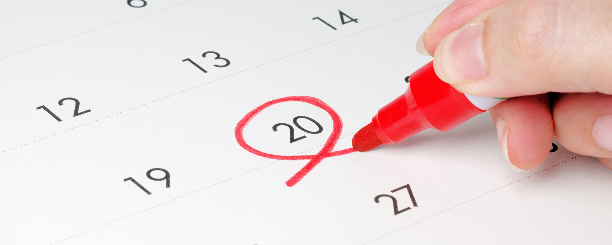 Eine Hand umkreist mit einem roten Stift die Zahl „20“ auf einem Kalenderblatt.