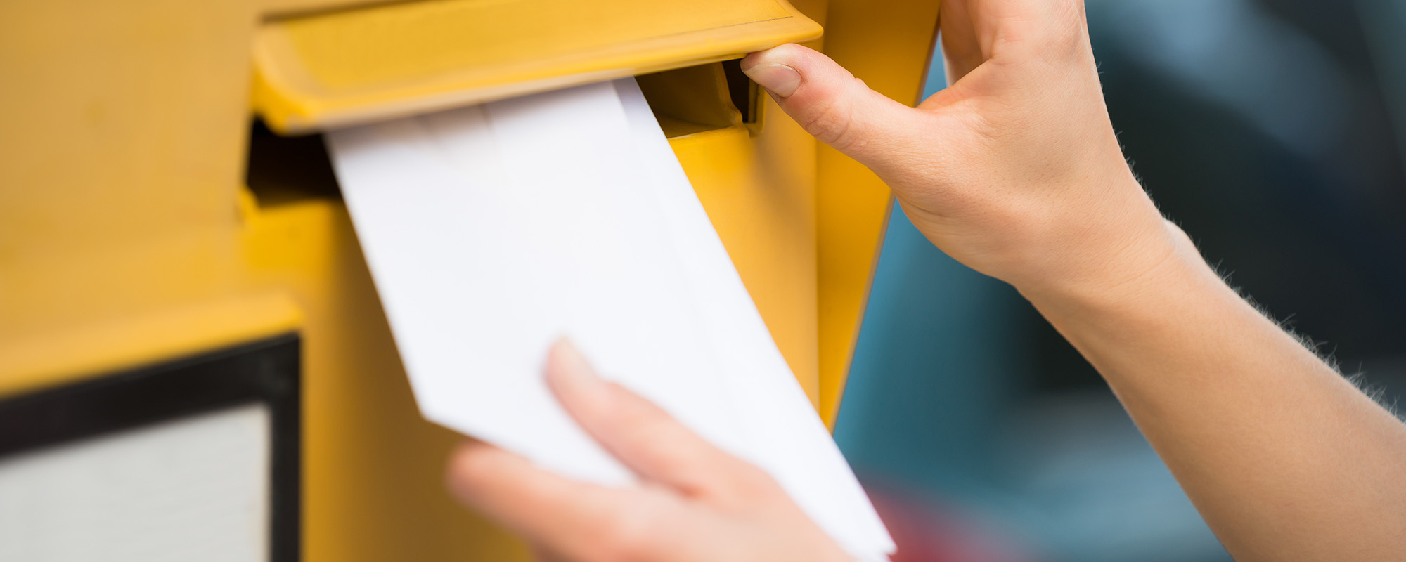 Im Bildausschnitt ist zu sehen, wie eine Person einen Brief in einen Briefkasten der Deutschen Post wirft.