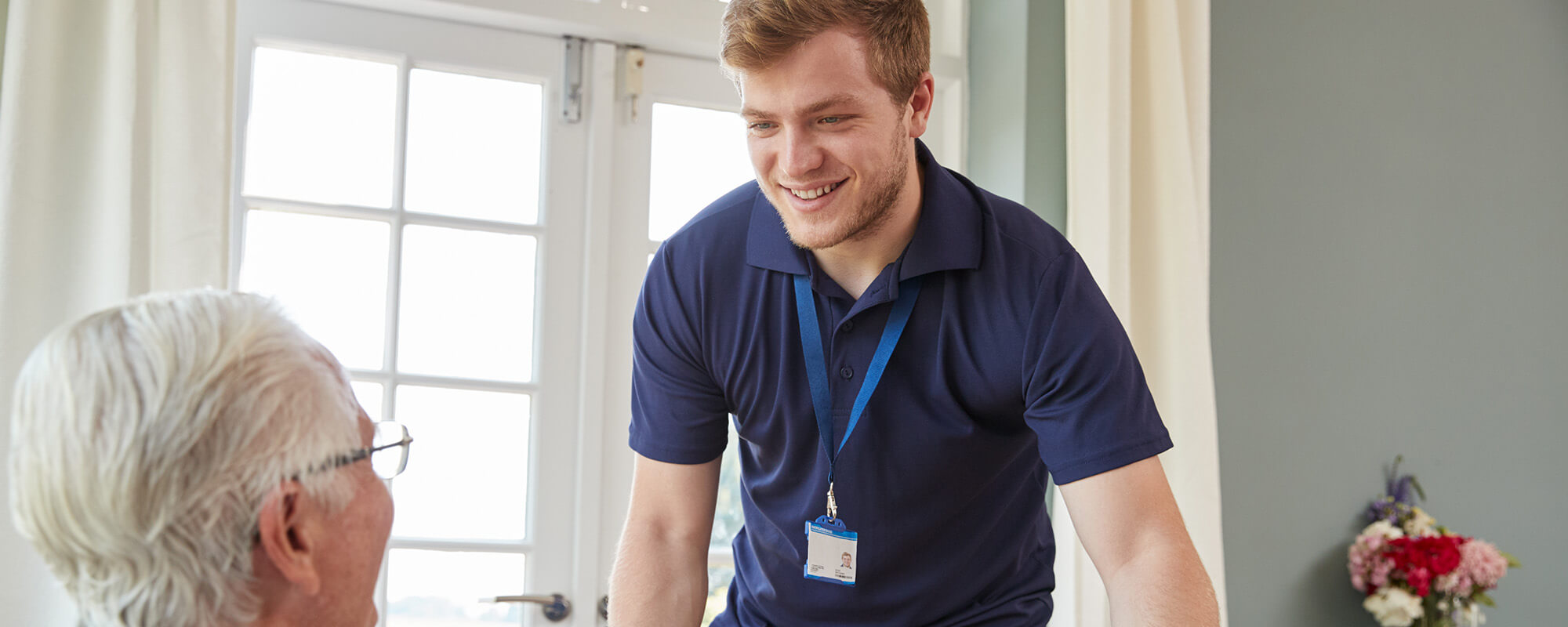 Ein junger Mann in einem blauen T-Shirt beugt sich zu einem älteren Mann. 