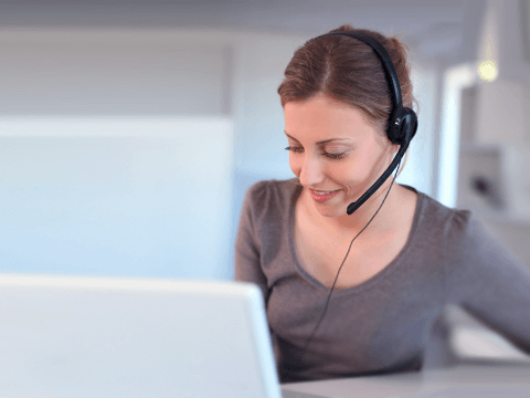 Frau sitzt mit Headset vor einem Laptop.