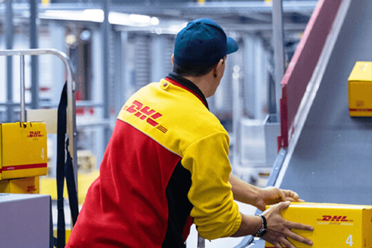 DHL Mitarbeiter legt Päckchen auf ein Fließband.