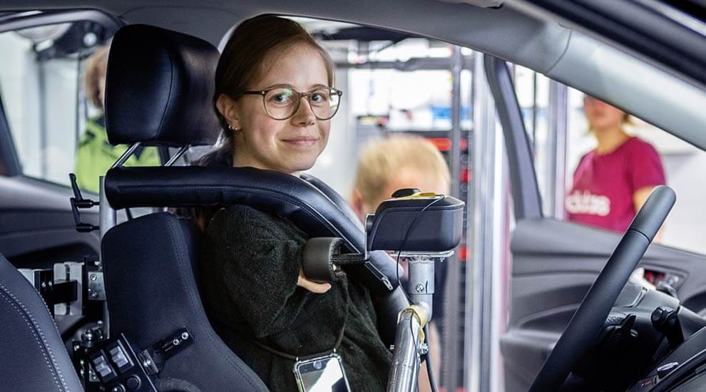 Eine junge Frau sitzt in einem behindertengerecht umgebauten Auto.
