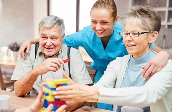 Eine junge Frau spielt mit zwei älteren Menschen. Alle lächeln.