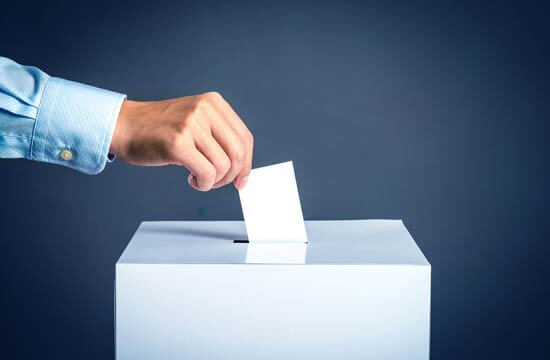 Ein Stimmzettel wird in eine Wahlurne geworfen.