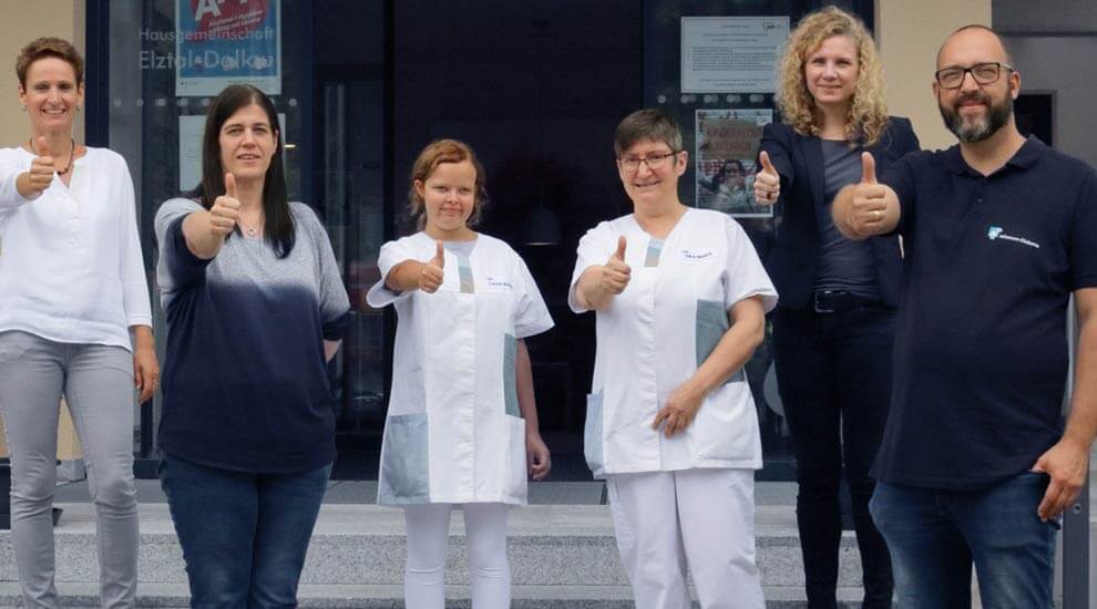 Gruppenbild. Sechs Menschen mit Carolin im Zentrum. Alle zeigen einen hochgereckten Daumen.