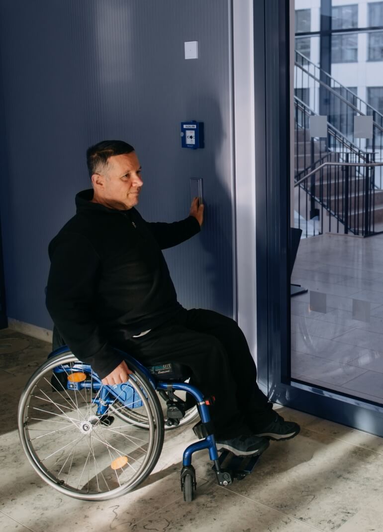 Mann im Rollstuhl betätigt einen Türöffner.