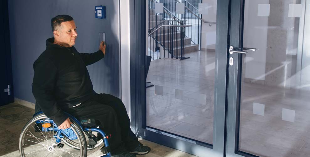 Mann im Rollstuhl betätigt einen Türöffner.