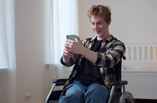 Mann im Rollstuhl lächelt in sein Smartphone.