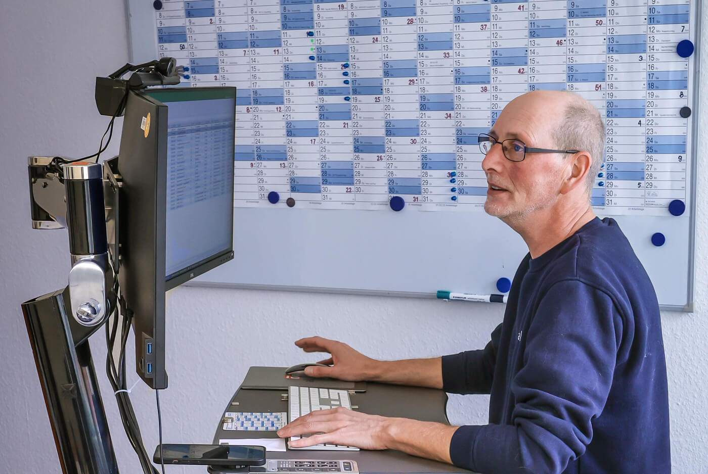 Carsten Schönebeck an seinem elektronisch verstellbaren Arbeitsplatz in sitzender Position.