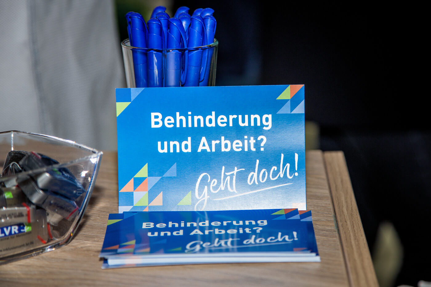 Nahaufnahme des Messestands  des LVR: Im Fokus steht eine aufgestellte Postkarte, auf der der Spruch "Behinderung und Arbeit? Geht doch!" aufgedruckt ist.