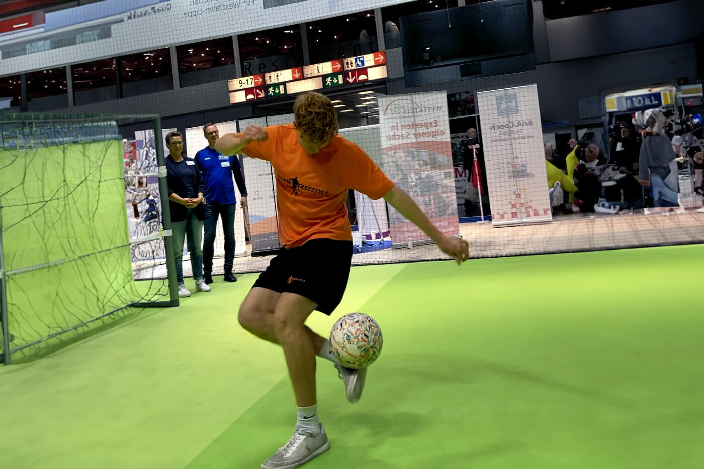 Ein junger Mann in Sportkleidung zeigt Fußballtricks auf dem beim Messestand aufgebautem Fußballfeld.