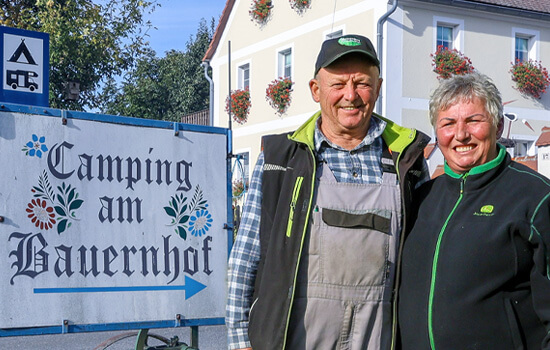 Das Ehepaar Leubner steht vor ihrem Hofschild "Camping auf dem Bauernhof"