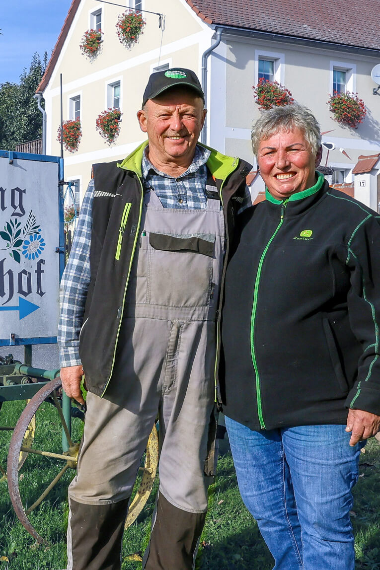 Das Ehepaar Leubner steht vor ihrem Hofschild "Camping auf dem Bauernhof"