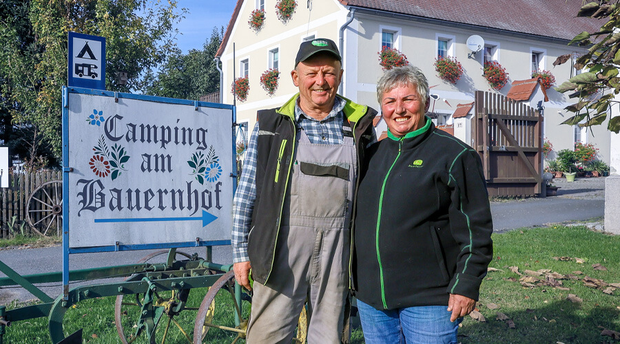 Das Ehepaar Leubner steht vor ihrem Hofschild "Camping auf dem Bauernhof"