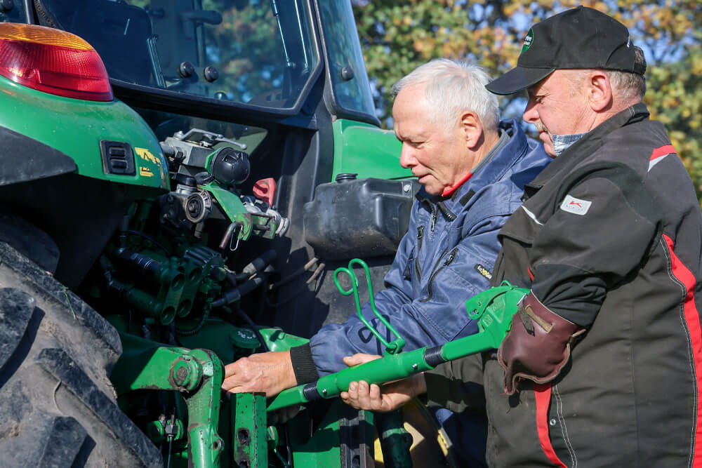 Wolfgang Leubner und seine Arbeitsassistenz stehen am Traktor und nehmen eine Einstellung vor.