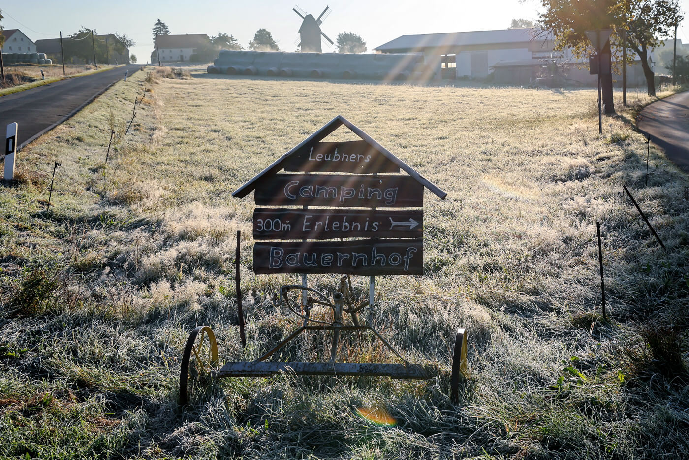 Die Sonne scheint auf eine raureifbedeckte Wiese, im Vordergrund einige Wegweiser. 