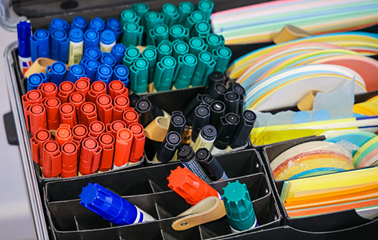 In einem Koffer mit Tagungsmaterialien leuchten farbenfrohe Stifte und bunte Karten in verschiedenen Formen und Größen.