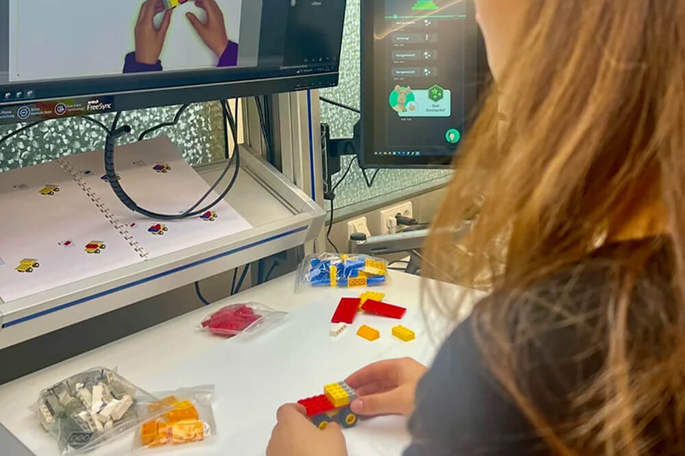 Eine Frau sitzt am Schreibtisch vor einem Computer und baut mit Legosteinen.